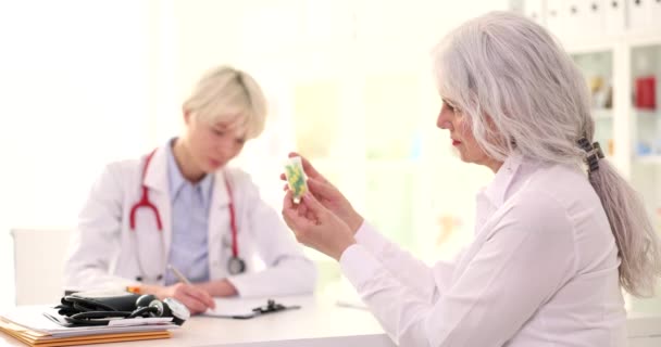 Una hermosa anciana en la clínica mira los medicamentos, un primer plano. El médico prescribe una prescripción - Imágenes, Vídeo