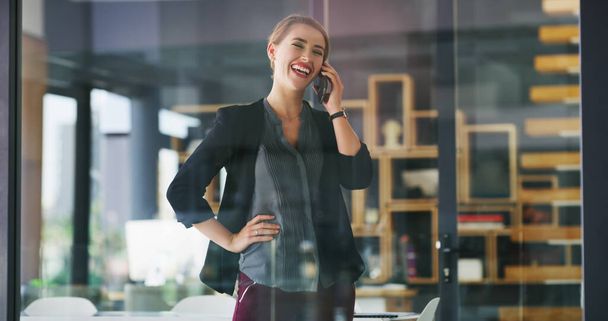 Заключаю сделку по телефону. привлекательная молодая деловая женщина, стоящая одна в своем офисе и разговаривающая по мобильному телефону - Фото, изображение