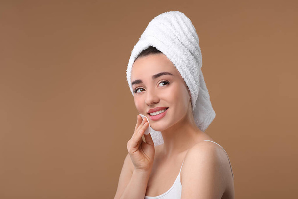 Beautiful woman in terry towel removing makeup with cotton pad on beige background, space for text - Фото, изображение