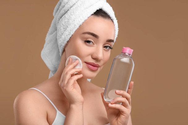 Beautiful woman in terry towel removing makeup with cotton pad on beige background - Φωτογραφία, εικόνα