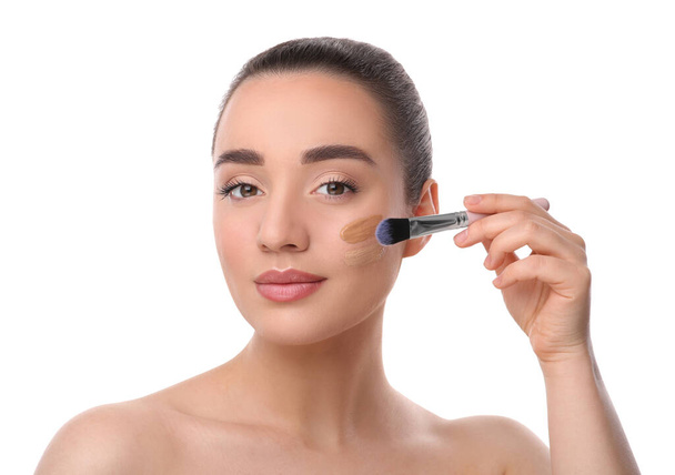 Woman applying foundation on face with brush against white background - Fotoğraf, Görsel