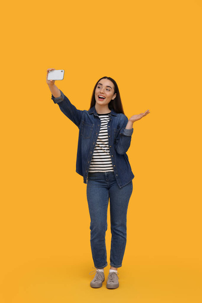 Smiling young woman taking selfie with smartphone on yellow background - Fotó, kép