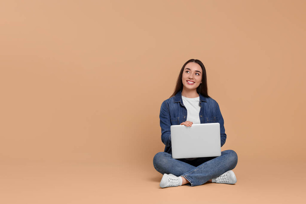 Smiling young woman with laptop on beige background, space for text - Foto, afbeelding