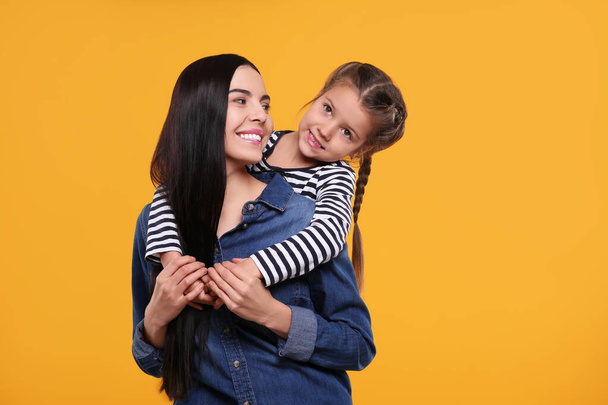 Happy woman with her cute daughter on yellow background. Mother's day celebration - Fotoğraf, Görsel