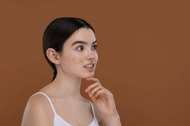 Teenage girl with swatch of foundation on face against brown background. Space for text - Foto, Bild