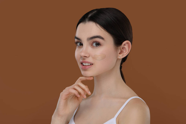 Teenage girl with swatch of foundation on face against brown background - Foto, immagini