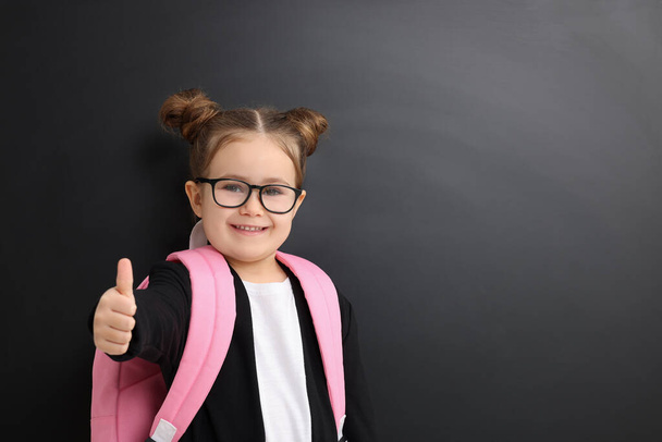 Happy little school child with backpack showing thumbs up near chalkboard. Space for text - Fotó, kép