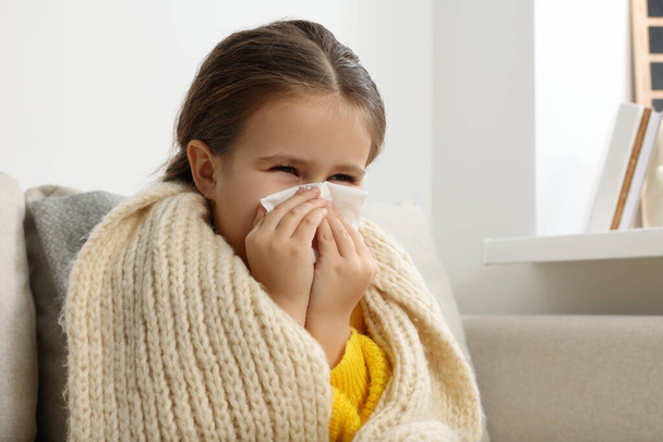 Girl blowing nose in tissue on sofa in room. Cold symptoms - Φωτογραφία, εικόνα