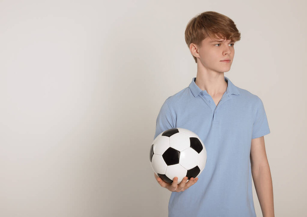 Хлопчик-підліток з футбольним м'ячем на світло-сірому фоні. Простір для тексту
 - Фото, зображення