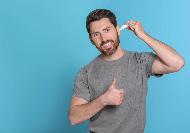 Man using ear drops and showing thumbs up on light blue background, space for text - Fotografie, Obrázek