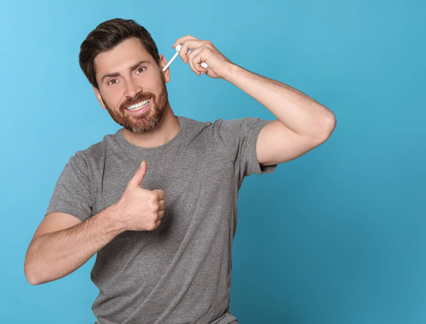 Man using ear spray and showing thumbs up on light blue background, space for text - Foto, Bild