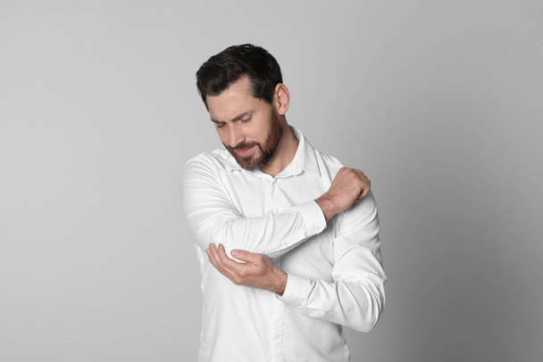 Man suffering from pain in his elbow on light background. Arthritis symptoms - Фото, изображение
