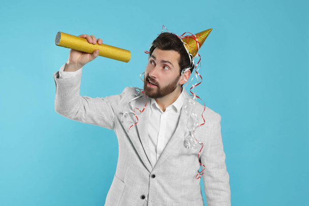 Handsome man with party popper on light blue background - Foto, imagen