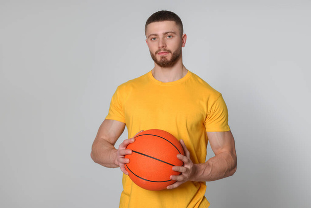 Athletic young man with basketball ball on light grey background - Photo, Image
