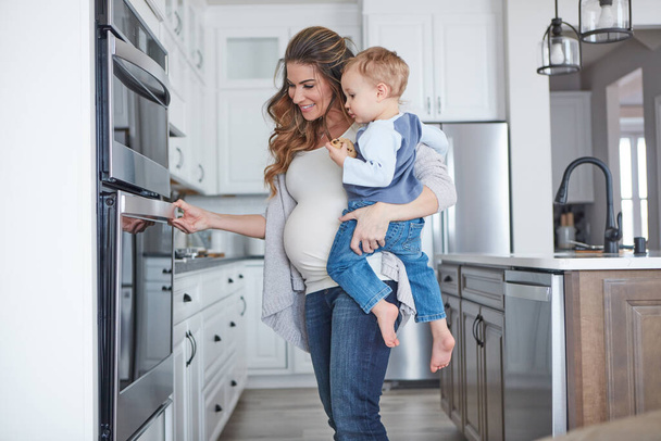No one can juggle like a mom does. a pregnant woman baking while spending spending time with her toddler son at home - 写真・画像