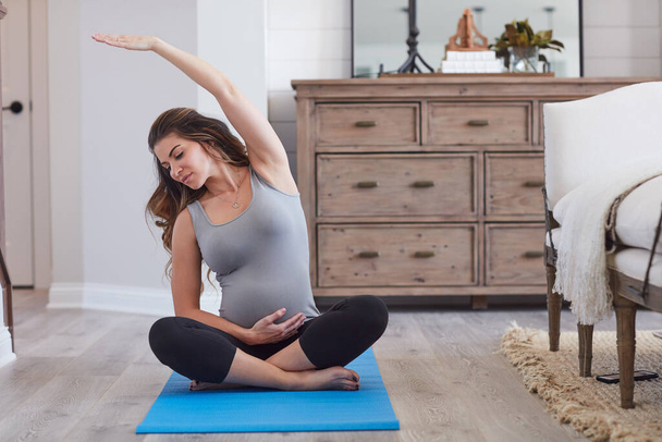 Das letzte Stück soll friedlich verlaufen. eine schwangere junge Frau praktiziert zu Hause eine Yoga-Routine - Foto, Bild