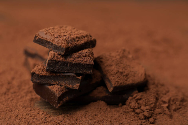 Pieces of tasty chocolate and cocoa powder on wooden table, closeup - Fotoğraf, Görsel