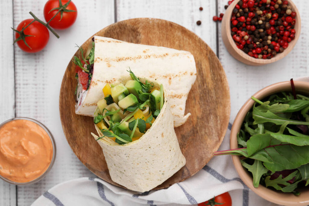Delicious sandwich wraps with fresh vegetables, sauce, tomatoes and peppercorns on white wooden table, flat lay - Photo, image