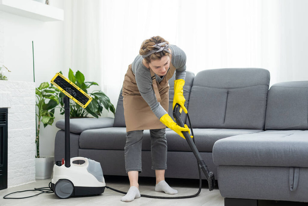 Женщина чистит диван с пылесосом дома
. - Фото, изображение