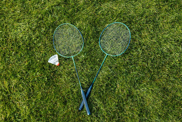 leisure games and sport equipment concept - close up of badminton rackets and shuttlecock on grass - 写真・画像