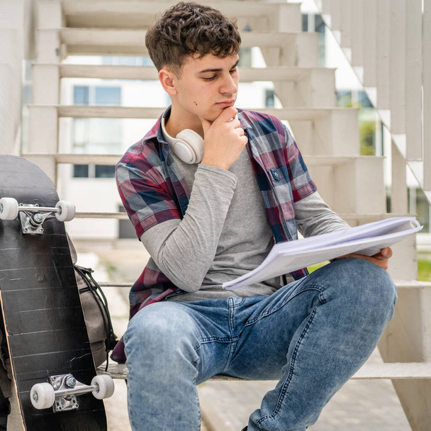 Een jonge man tiener Kaukasische student met boeken lees studie op de campus in de dag zitten op trap onderwijs concept kopiëren ruimte - Foto, afbeelding
