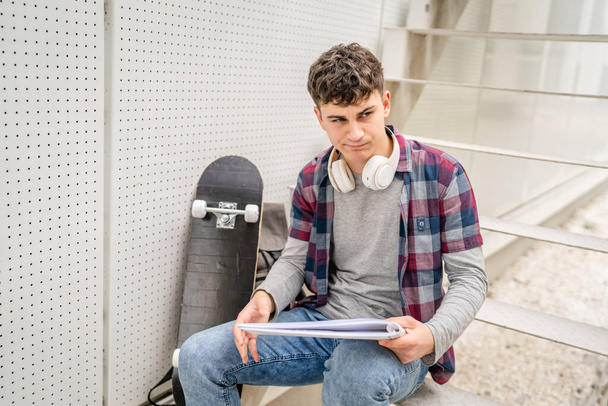 Um jovem adolescente estudante caucasiano com livros ler estudo no campus no dia sentar na escada educação conceito copiar espaço - Foto, Imagem