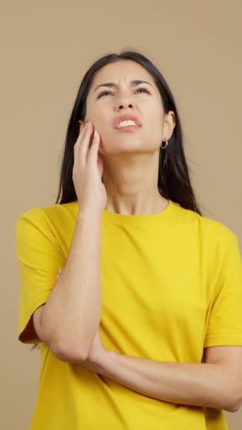Латиноамериканка с рукой на лице и вдумчивым выражением лица в студии с коричневым фоном - Кадры, видео