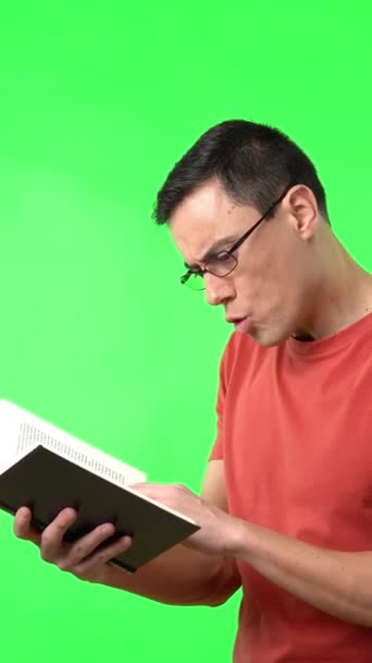 Astonished intelligent male in eyeglasses reading book and expressing amazement with opened mouth on chromakey - Materiał filmowy, wideo