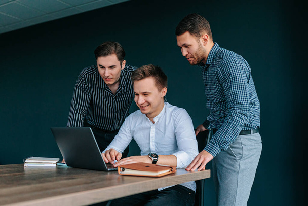Egy csapat három fiatal irodai munkás, köztük egy asszisztens, egy menedzser és egy kolléga, mind keményen dolgoznak a laptopjukon, hogy biztosítsák cégük sikerét.. - Fotó, kép