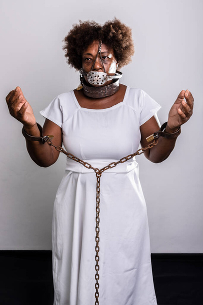 Portrait of a black woman in chains with an iron mask over her mouth. Slavery in Brazil. Arms in prayer. Studio reproduction. - Fotografie, Obrázek