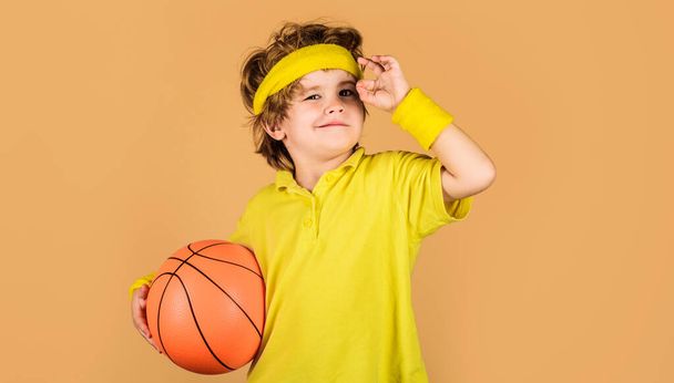 Χαμογελώντας παιδί με μπάλα μπάσκετ δείχνει σημάδι εντάξει, εξαιρετικό σύμβολο. Παιχνίδι μπάσκετ. Παιδικές δραστηριότητες. Μικρέ μπασκετμπολίστα. Αθλητικός εξοπλισμός. Παιδική ηλικία και σπορ. Το παιδί παίζει μπάσκετ με μπάλα μπάσκετ. - Φωτογραφία, εικόνα