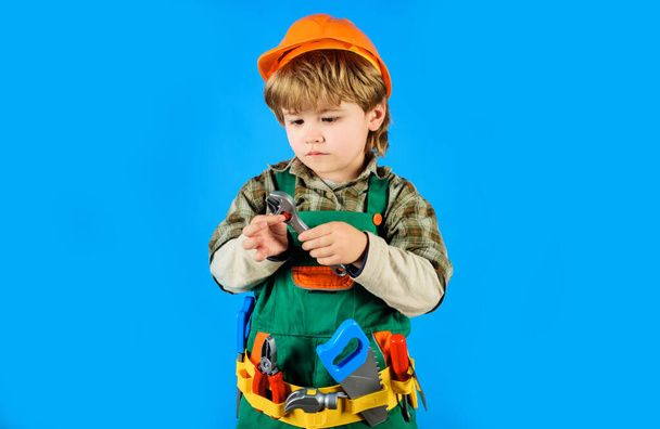 Ремонтник с гаечным ключом. Ребенок в форме строителя и строительном шлеме с регулируемым гаечным ключом. Инструменты для строительства. Маленький строитель с поясом. Ремонтник играет с инструментом для ремонта - Фото, изображение