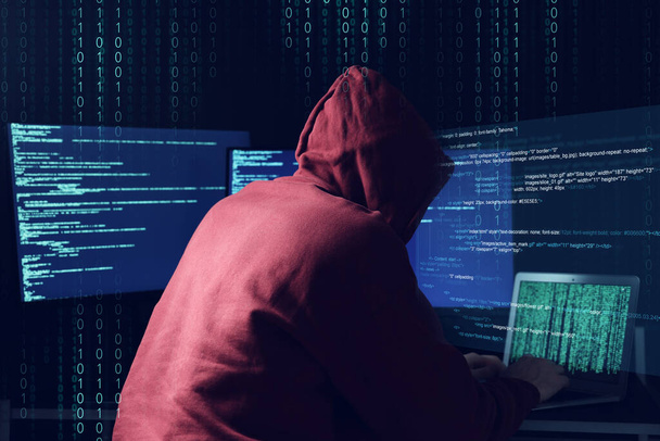 Cyberatak. Anonimowy haker pracujący z laptopem i monitorami na ciemnoniebieskim tle. Kod binarny wokół niego - Zdjęcie, obraz