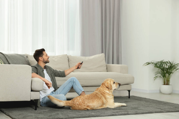 Hombre encendiendo la televisión cerca de su lindo Labrador Retriever en casa - Foto, Imagen