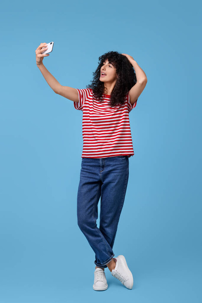 Beautiful young woman taking selfie on light blue background - Zdjęcie, obraz