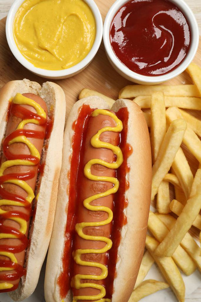 Delicious hot dogs with mustard, ketchup and potato fries on table, flat lay - Foto, imagen