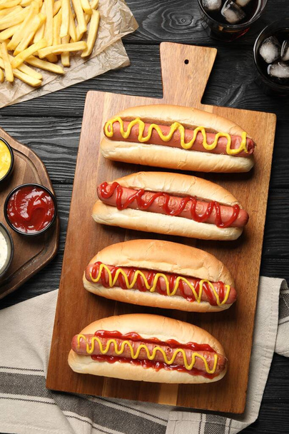 Delicious hot dogs with mustard, ketchup and potato fries on black wooden table, flat lay - Photo, image