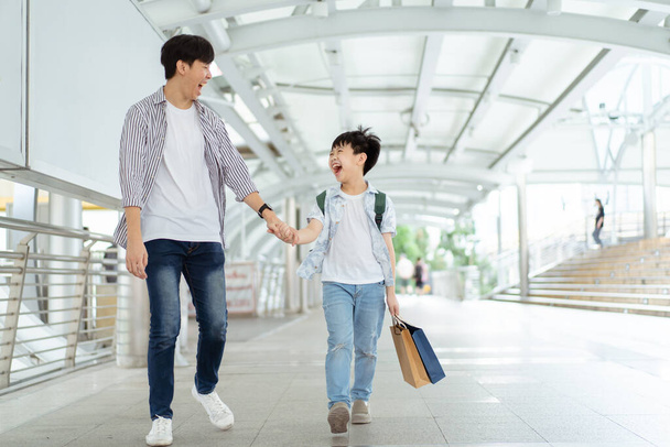 Père emmenant son fils à l'école et faisant du shopping, un homme tenant la main d'un enfant tout en marchant ensemble dans le quartier du centre-ville. - Photo, image