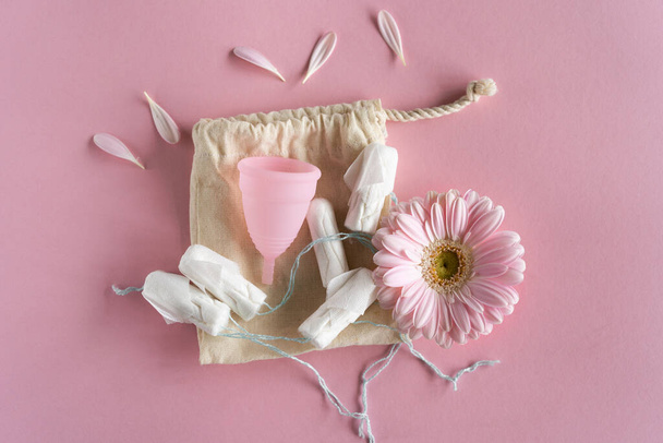 Tampony i kubek menstruacyjny na różowym tle. Kubek menstruacyjny vs tampony. Zero odpadów i koncepcja ekożycia - Zdjęcie, obraz