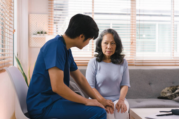 Une jeune aidante consulte une femme âgée asiatique de 60 ans, ce qui l'encourage et lui donne des antécédents médicaux. Les deux sont montrés se tenant la main et échangeant des mots d'encouragement - Photo, image