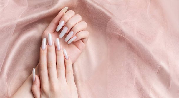 Manikürlü bir kadının elleri, tırnakları beyaz bir renge boyanır. Pembe ipek arkaplan - Fotoğraf, Görsel