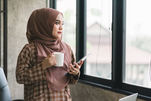 Schöne muslimische Geschäftsfrau im Hidschab arbeitet fleißig an ihrem Tablet und zeigt Professionalität und Engagement für ihren Job - Foto, Bild