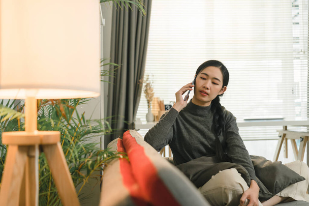 Okouzlující asijské žena je pomocí svého smartphonu při relaxaci na pohovce doma - Fotografie, Obrázek