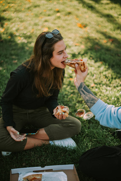 公園で草の上に座っている間に彼の女の子のピザのスライスを与える男の子 - 写真・画像