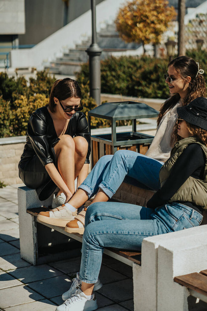 Three smiley happy girls sitting on a bench, enjoying the sunny weather. They are having a conversation and smiling - Foto, imagen