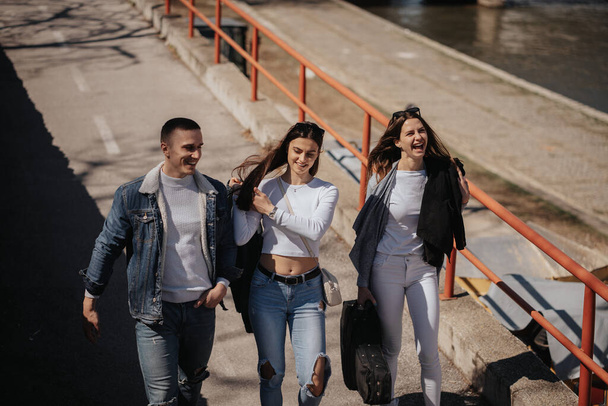 Primo piano di tre migliori amici che ridono mentre camminano vicino al fiume in città - Foto, immagini