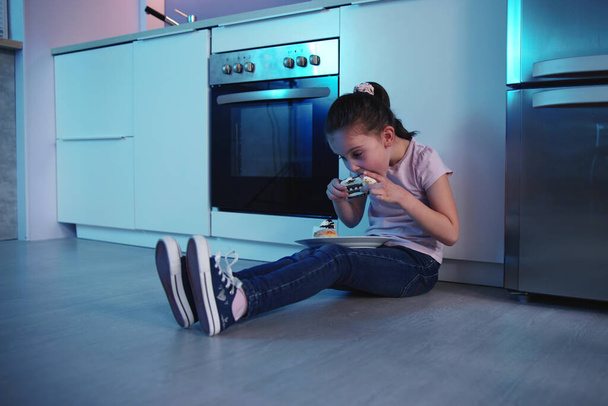 Child Eating Cake At Night Near Refrigerator - 写真・画像