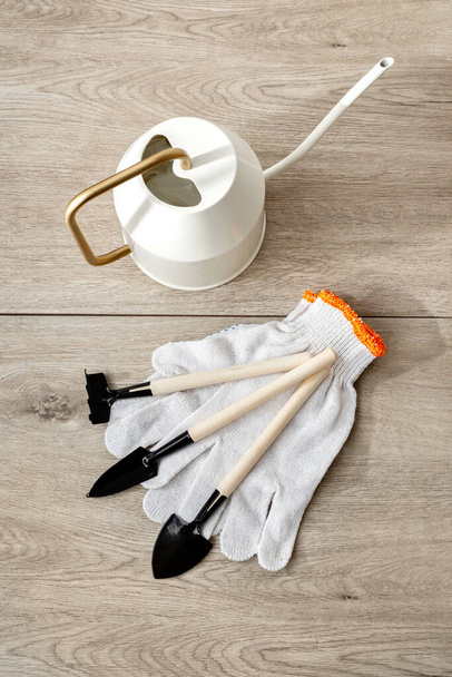 Indoor gardening hand tools set, watering can, small spades, rake and gloves on a beige wooden floor background, garden work concept - Photo, Image