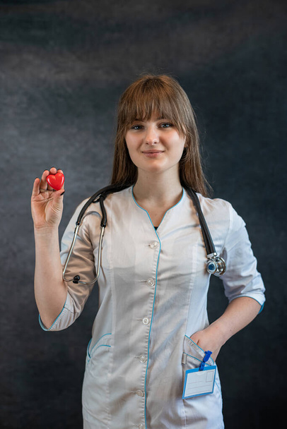 Female nurse in uniform with the stethoscope holding small red heart. We care concepts. - Foto, Imagen