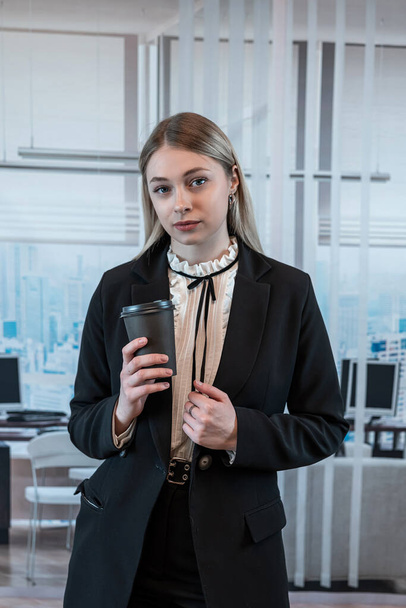 Geschäftsfrau im Anzug hält Kaffee und ruht sich allein im Flur des Business Centers aus, Mittagspause - Foto, Bild